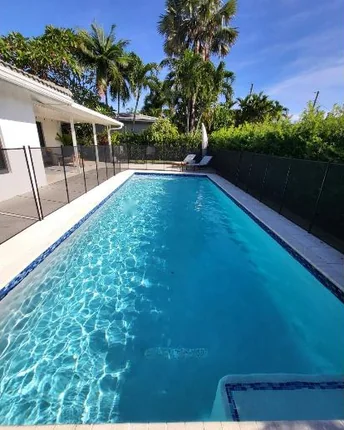 A rectangular family pool with safety fencing, clear blue water and a covered patio alongside.